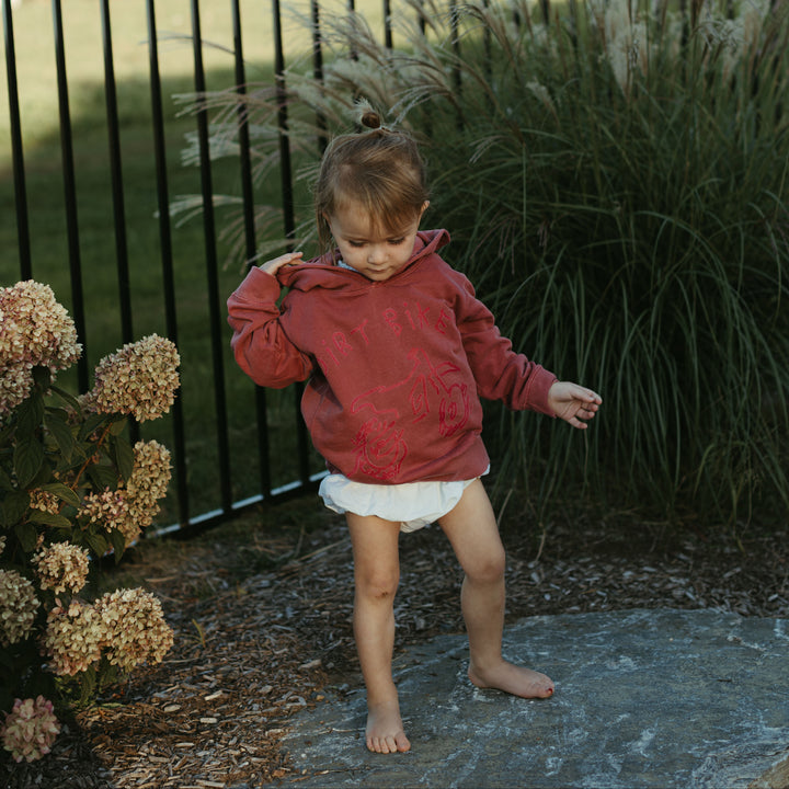 Child in a red jacket standing outdoors near a fence and plants