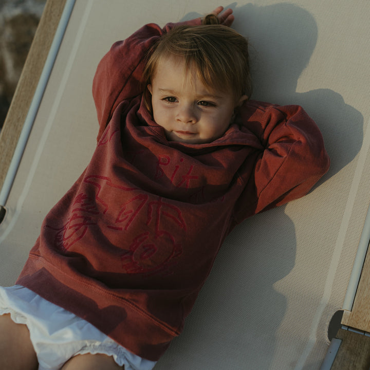 Child wearing a red dirt bike sweatshirt with white trim lying on a white surface.